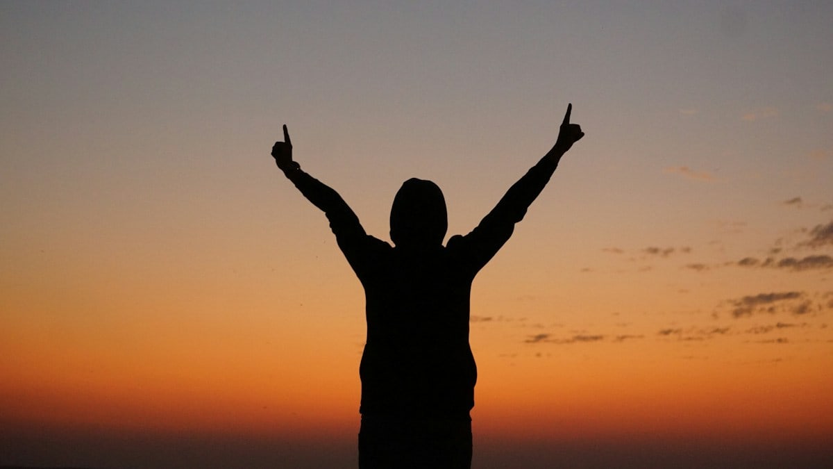 a person with their arms in the air at sunset